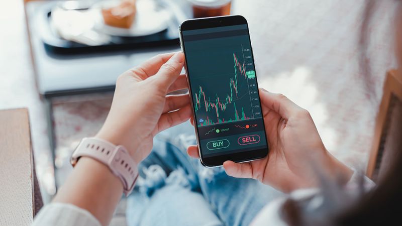 Person analyzing stock market data on a smartphone app, ready to buy or sell stocks.